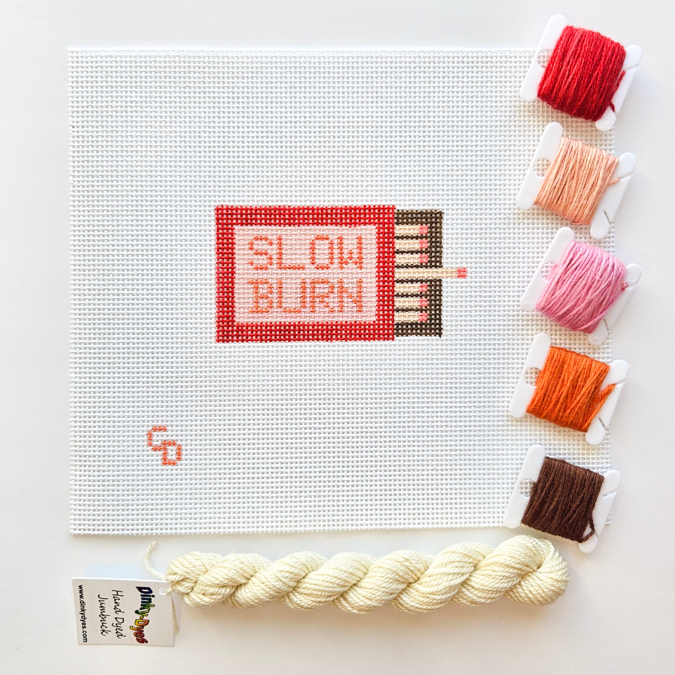 Needlepoint kit with 'Slow Burn' design and colorful threads on a white background