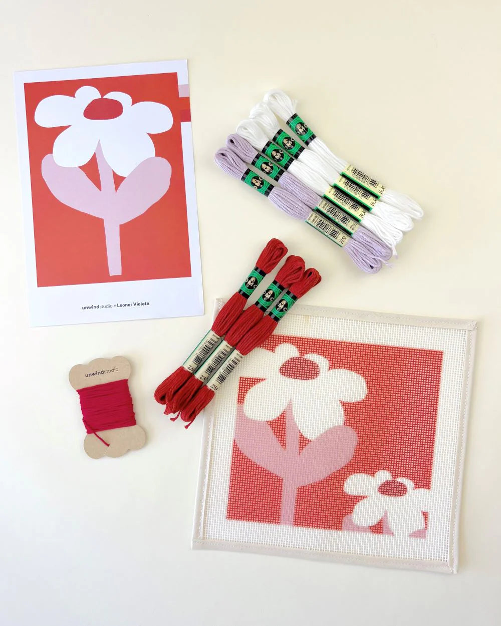 Needlepoint kit with red and white flower patterns, threads, and a cardboard flower template on a light background.