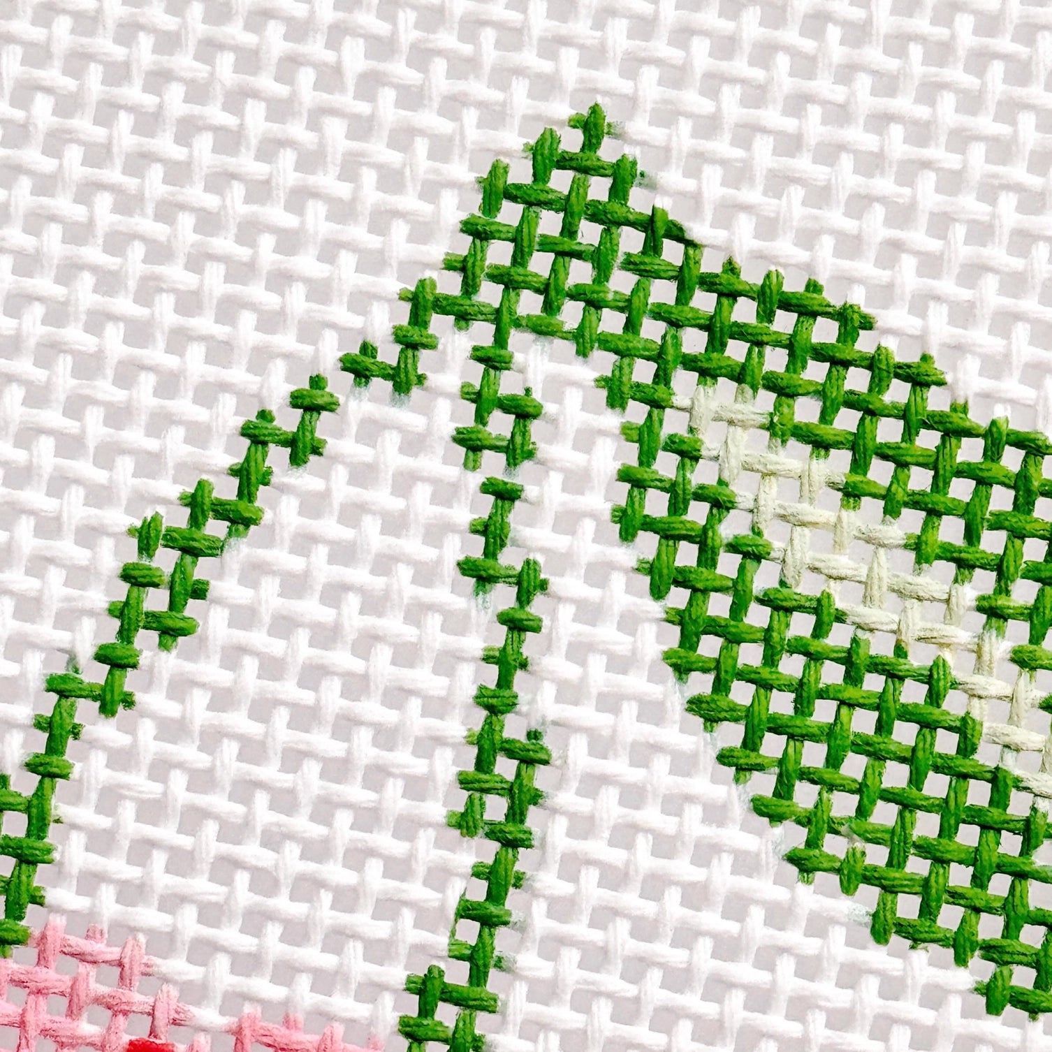 Needlepoint design with green thread on a white fabric background