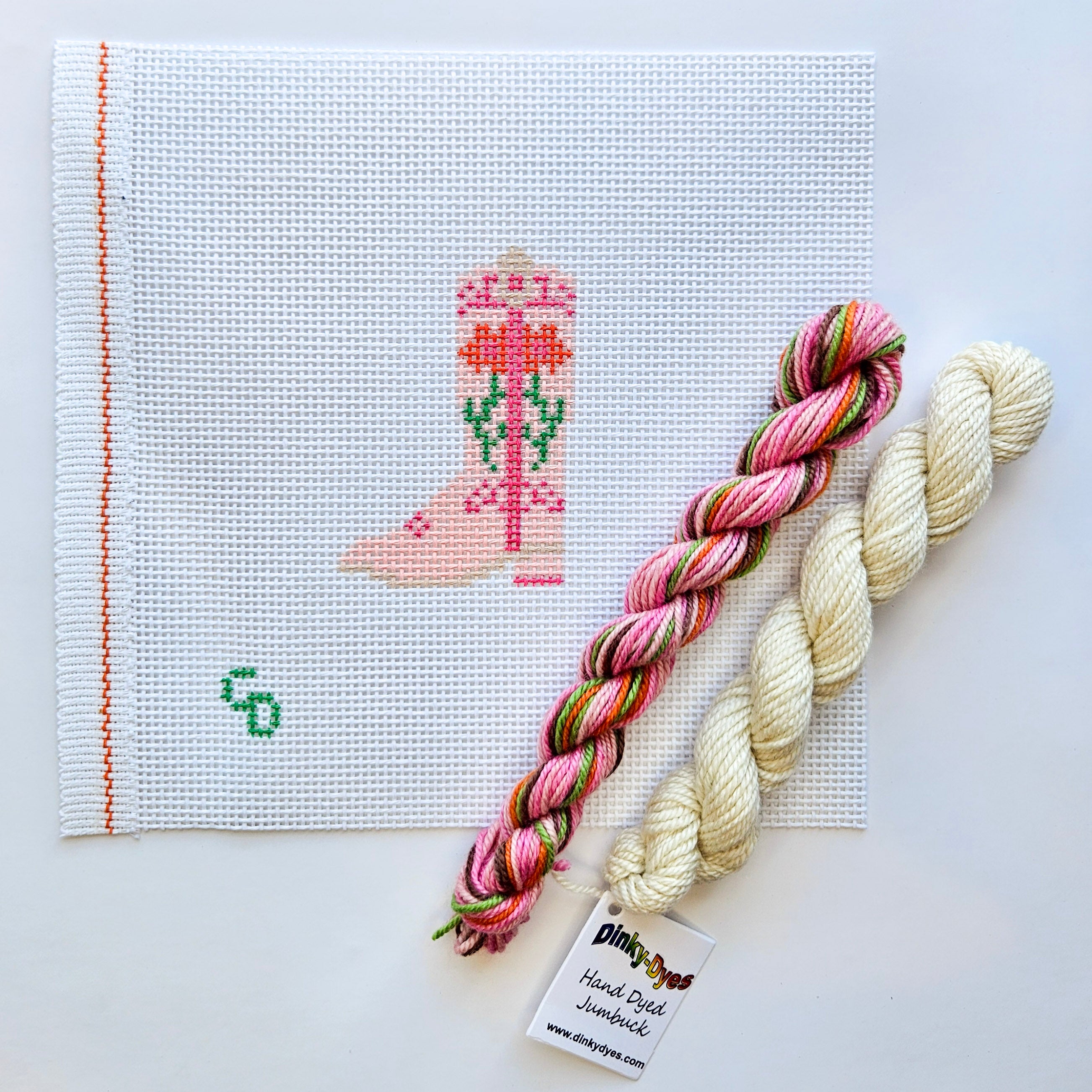 Needlepoint boot pattern on fabric with two skeins of yarn on a white background
