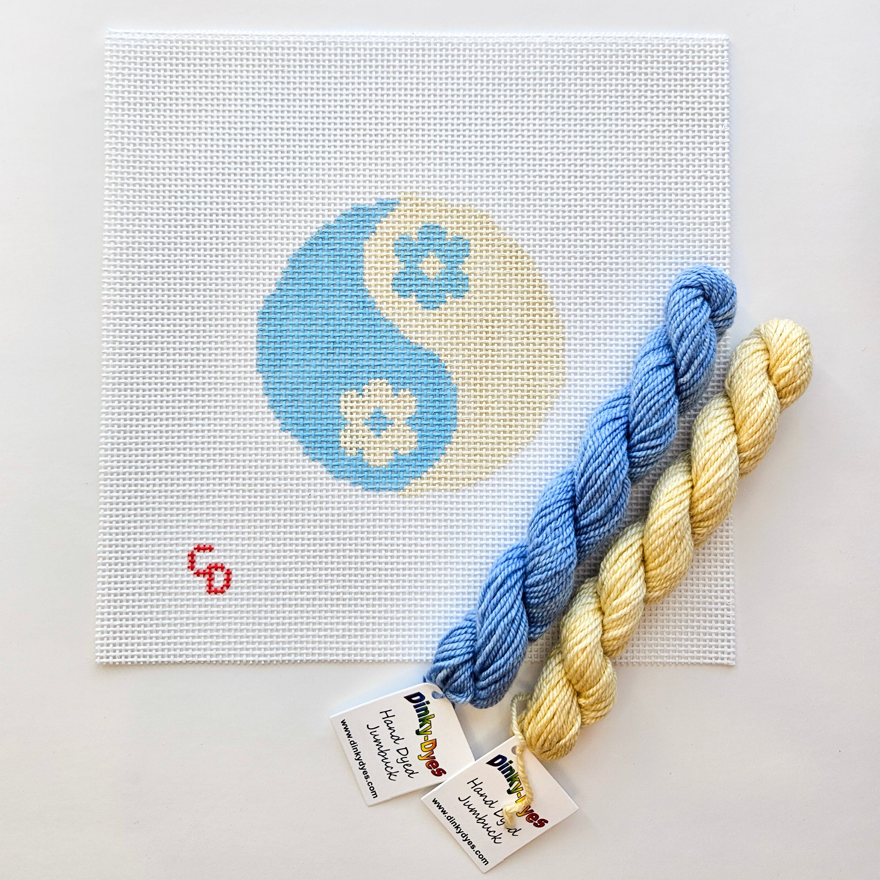 Two skeins of yarn, one blue and one yellow, with a needlepoint yin yang design in the background.