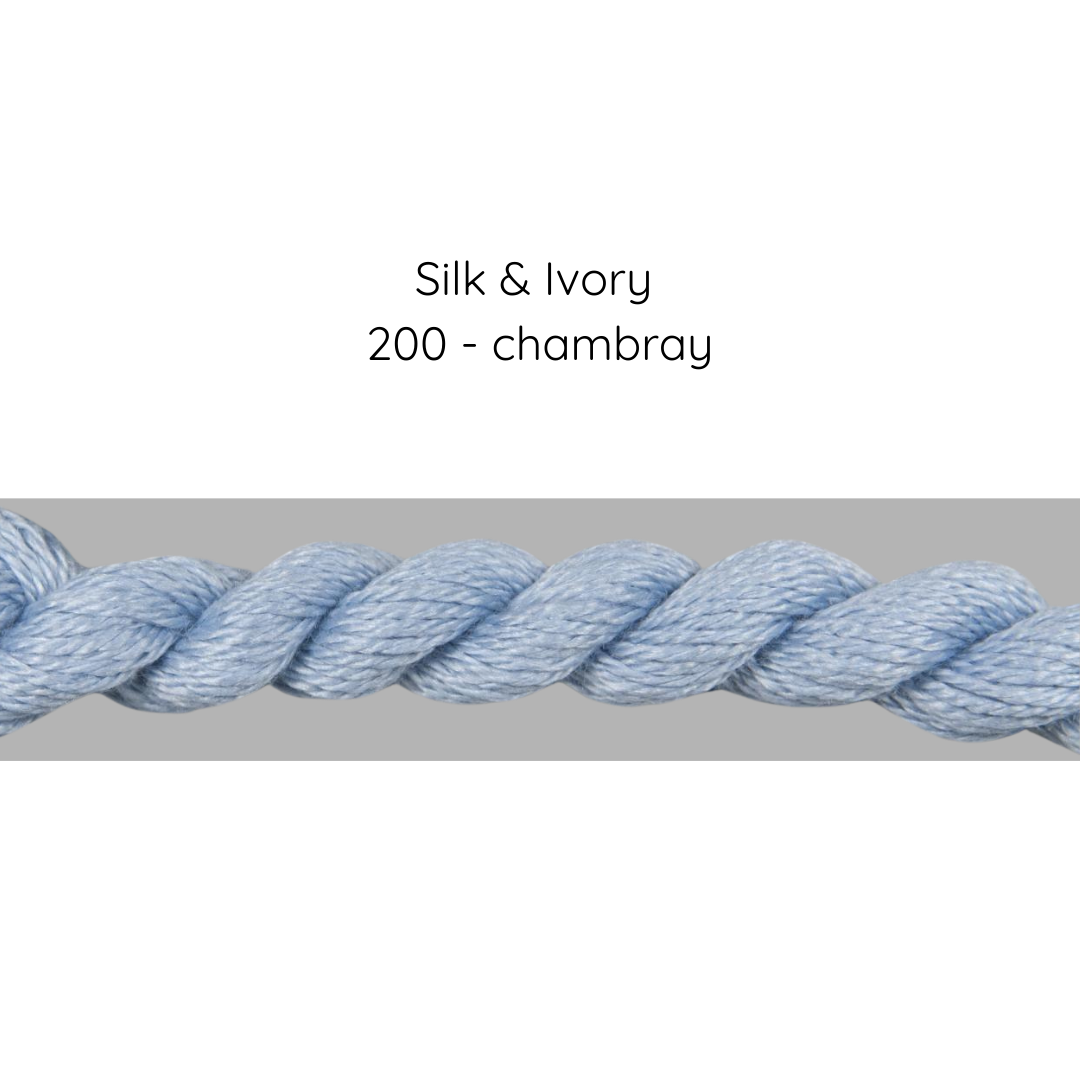 Close-up of blue yarn labeled 'Silk & Ivory 200 - chambray' on a gray background
