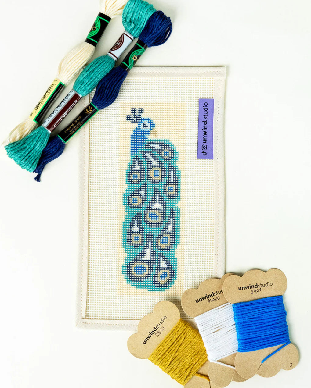 Needlepoint kit with threads and a peacock design on a white background